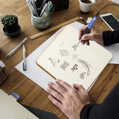 Person using a stylus to draw on a notebook with a wooden desk in the background