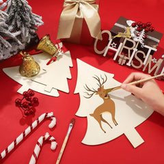 Person painting a reindeer design on a Christmas-themed card with festive decorations around.