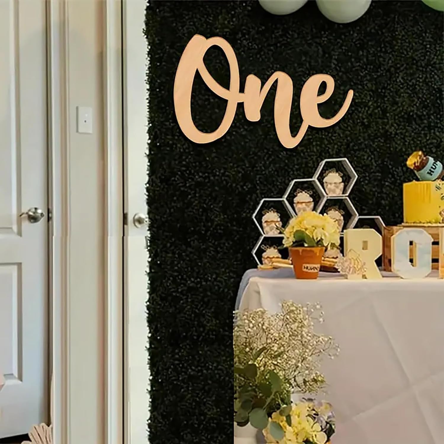 Decorative setup with 'One' sign on a black textured wall, table with flowers and decor items.