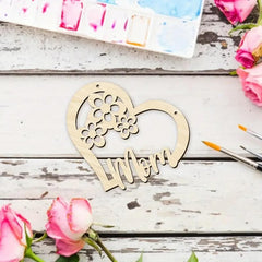 Wooden heart-shaped decoration with 'Mom' engraved, surrounded by pink roses on a rustic wooden surface.