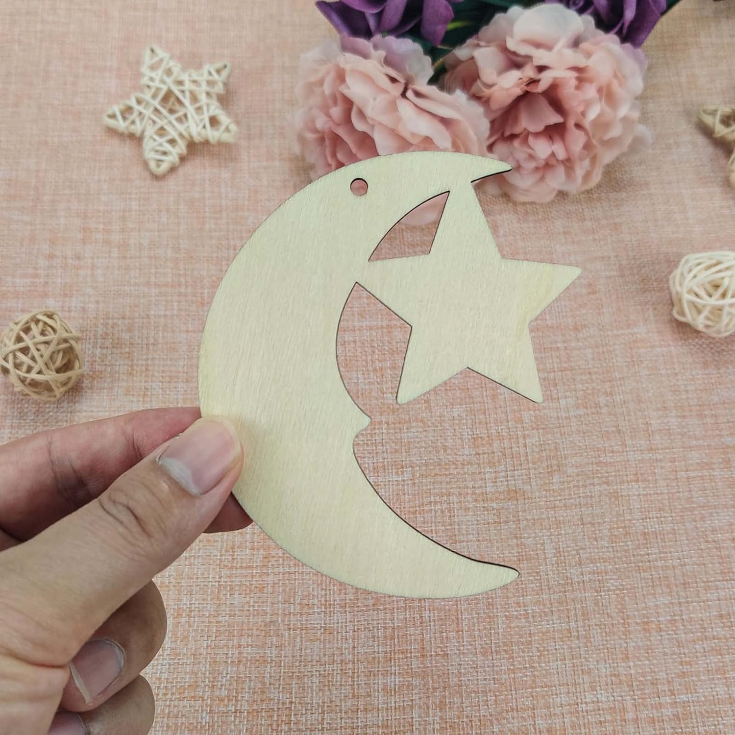 Wooden moon and star ornament held by a hand on a textured surface with flowers and decorative elements.