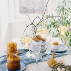 Decorative table setting with pastries, glasses, and small lights on a light background