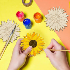 Hands painting a sunflower craft on a colorful background with paint containers and wooden sunflower templates.