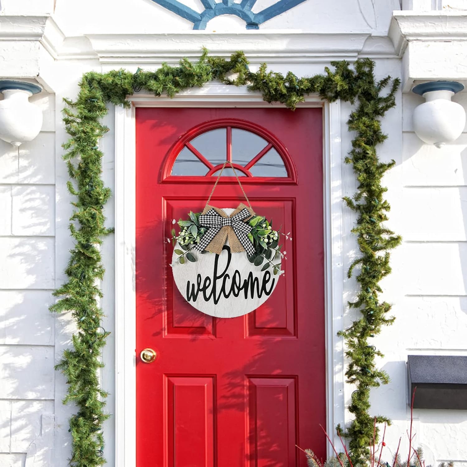 Red door with 'welcome' sign and greenery on a white house exterior