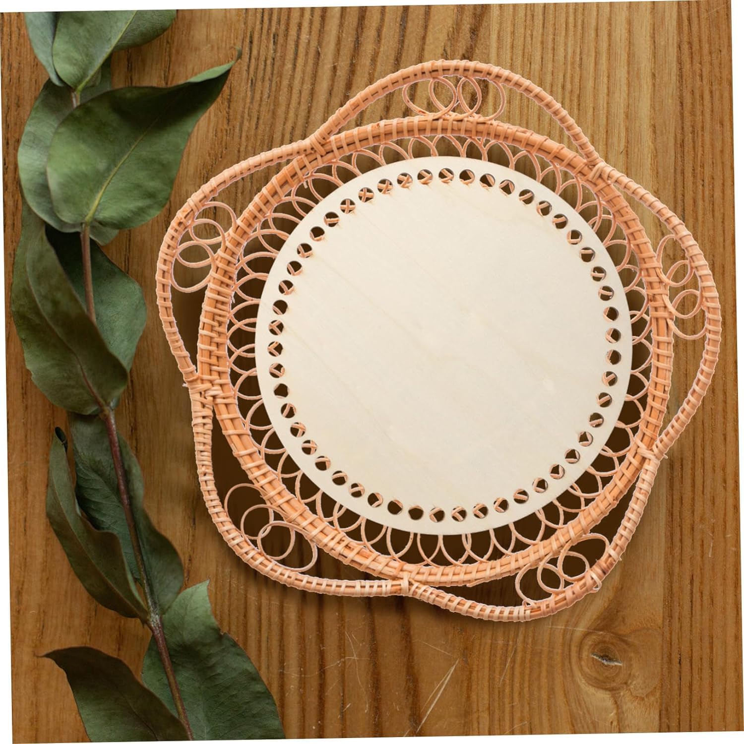 Set of woven placemats on a wooden surface with green leaves.
