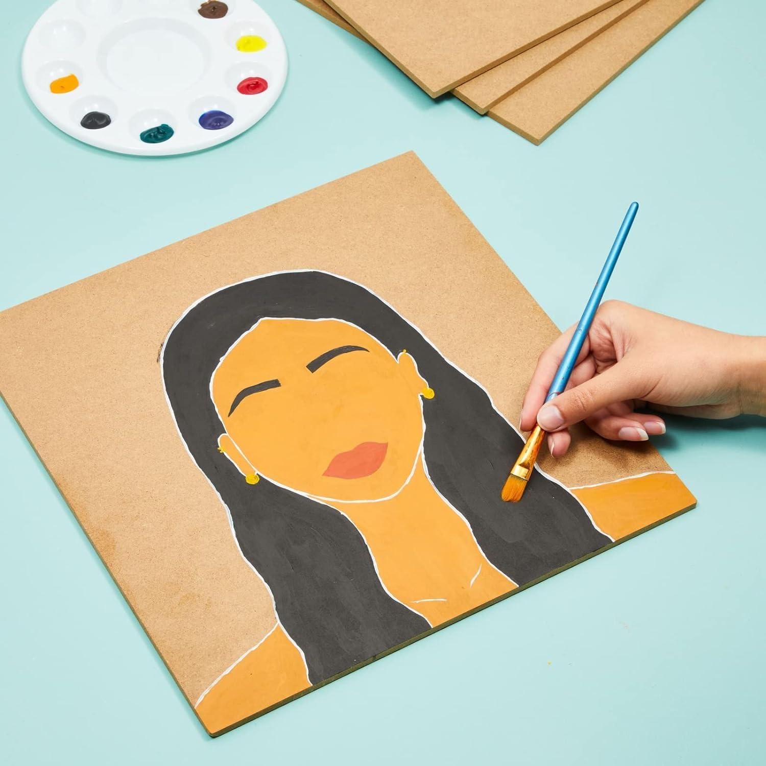 Person painting a portrait on brown paper with a paintbrush and color palette on a light blue background