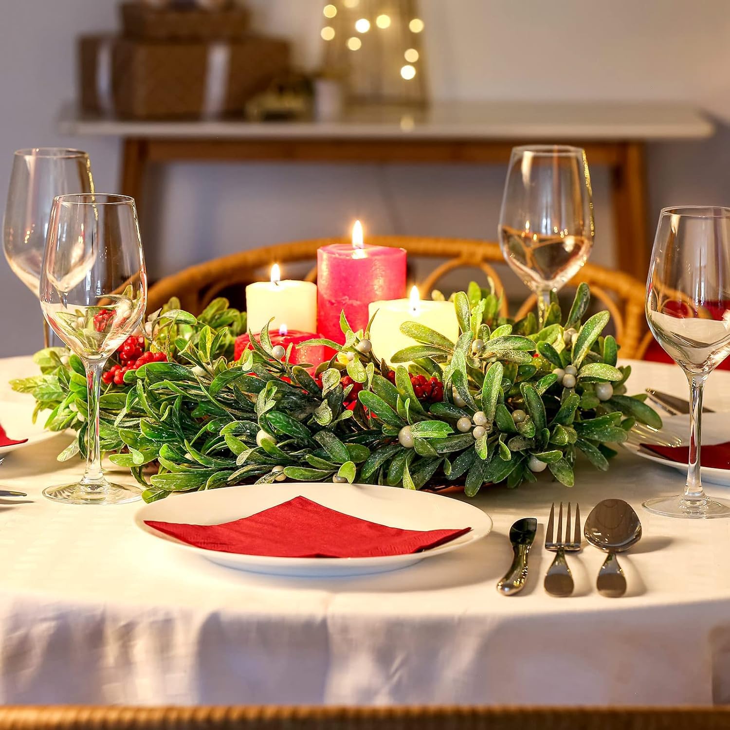 Dining table set for a festive meal with candles, glasses, and a wreath.