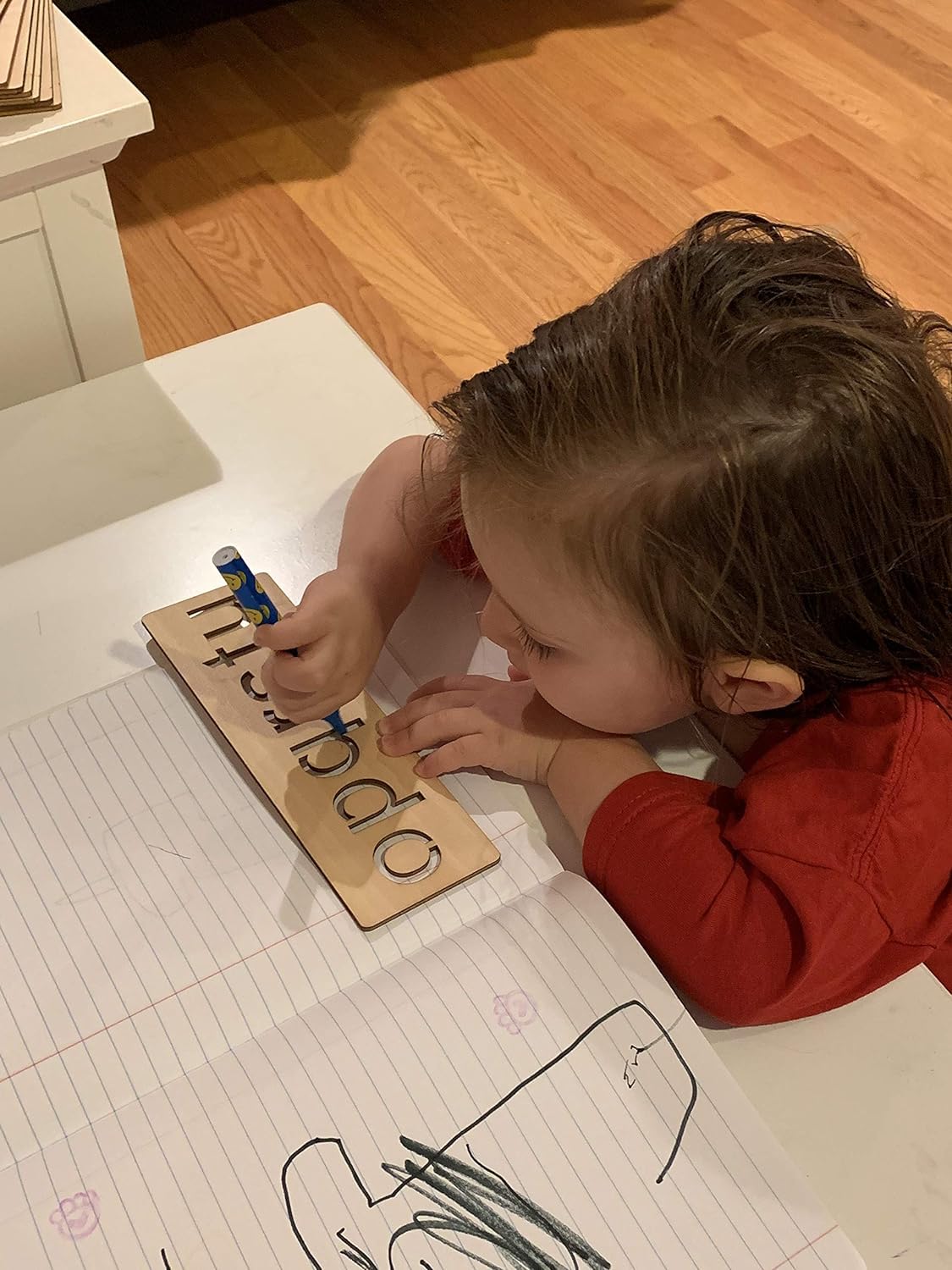 Child learning letters on a wooden alphabet board at a desk.