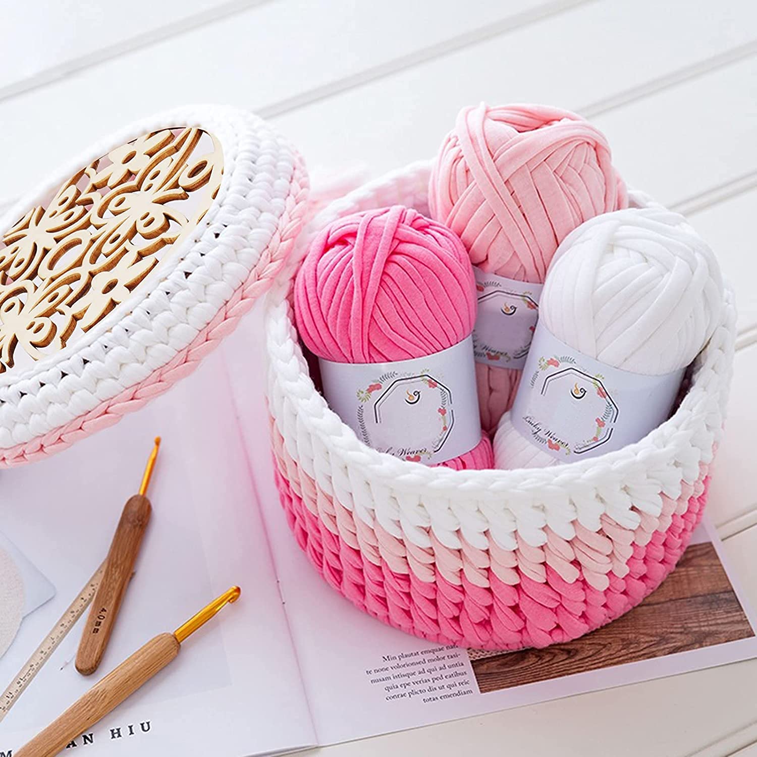 Basket with pink and white yarn balls and crochet hooks on a wooden surface