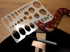 Metal template with holes, marker, and clamps on a wooden surface