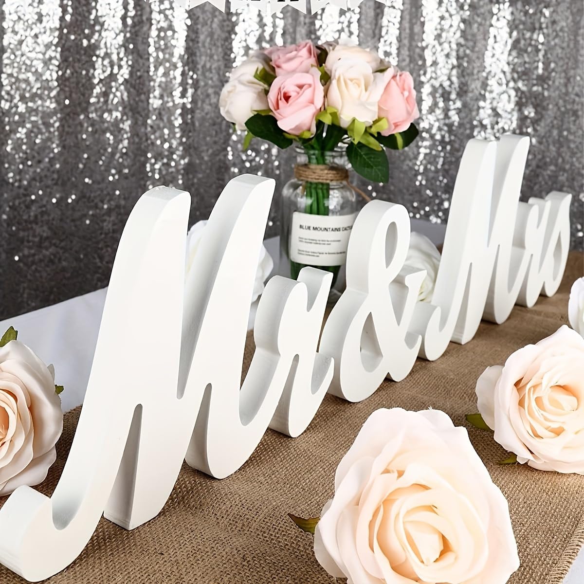 Decorative sign with 'Mr & Mrs' on a tablecloth with flowers and a sequin curtain background
