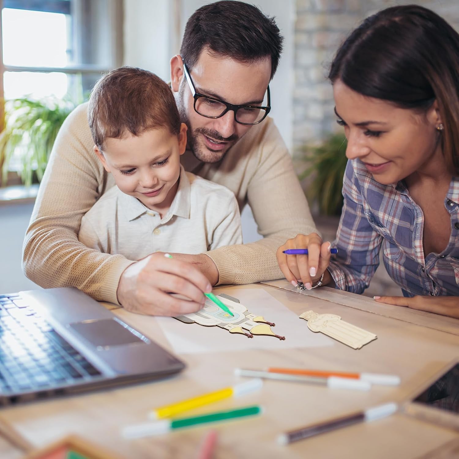 Family of three engaged in a craft activity at a table with colorful pens and paper.