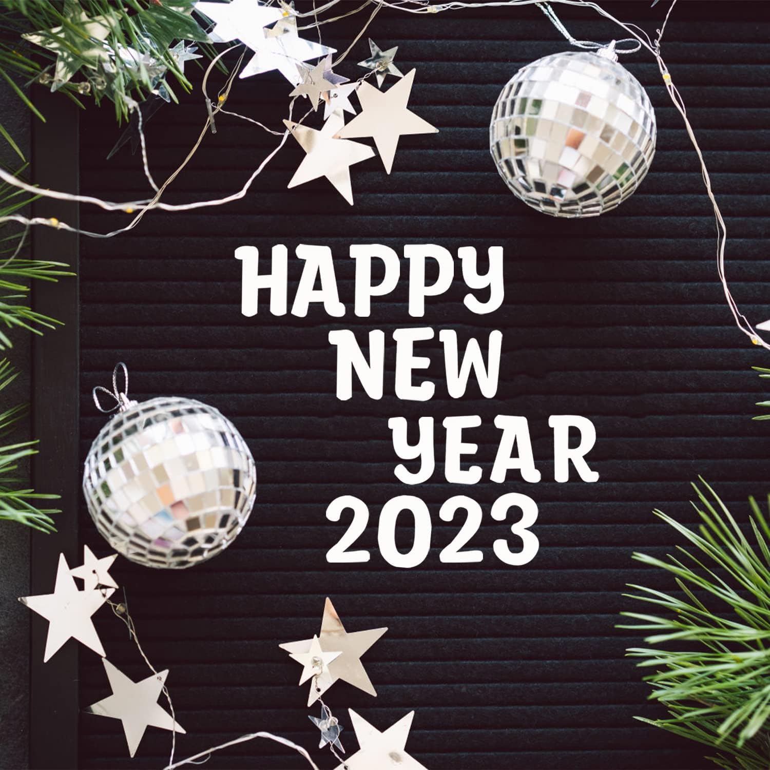 Happy New Year 2023 text on a black board with decorative ornaments and lights.
