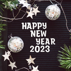 Happy New Year 2023 text on a black board with decorative ornaments and lights.