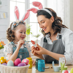 Woman and child wearing bunny ears, engaging in Easter egg decorating activity.