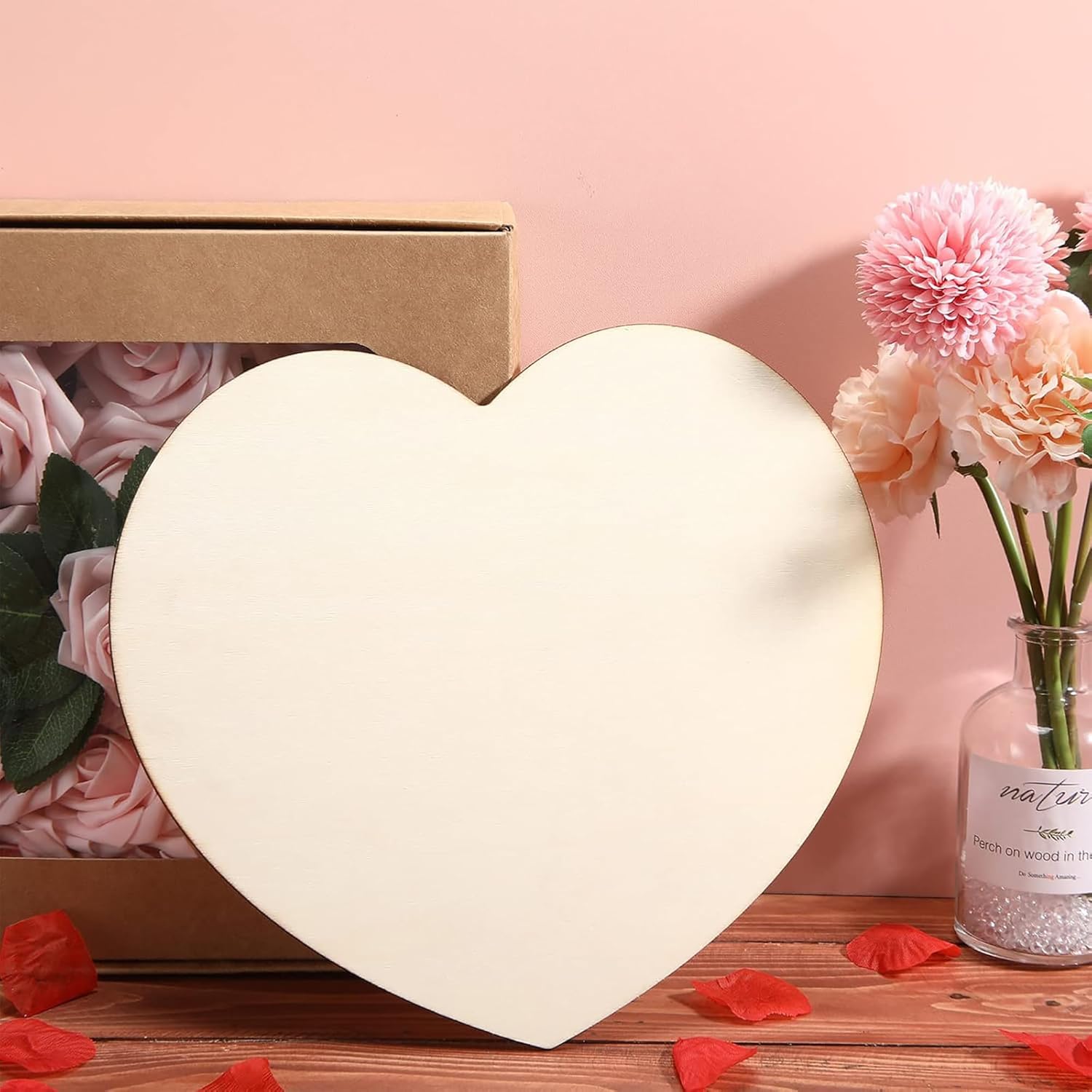 Heart-shaped box, pink flowers, and a vase on a wooden surface with a pink background