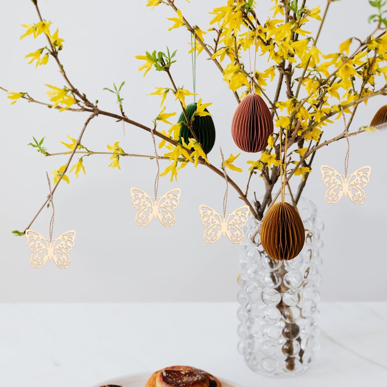 Decorative arrangement with yellow flowers, paper butterflies, and a clear vase on a light background