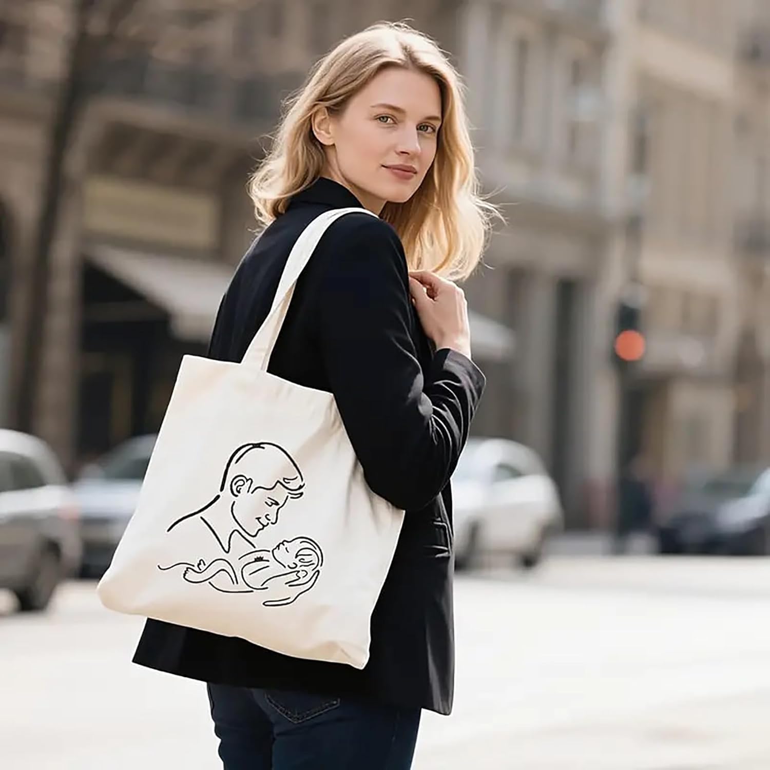 Woman holding a tote bag with a design of a woman holding a baby on a city street.