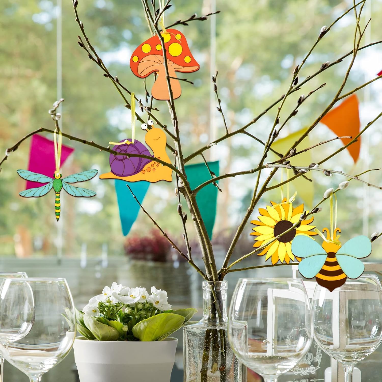 Decorative wooden cutouts of a mushroom, butterfly, dragonfly, bee, and sunflower hanging on branches with a blurred outdoor background.