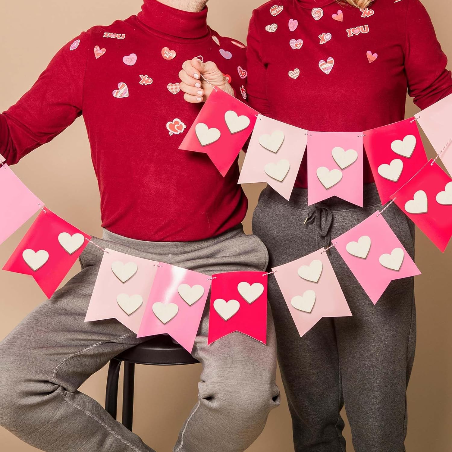 Two people wearing red shirts with heart patterns holding a heart-themed banner.