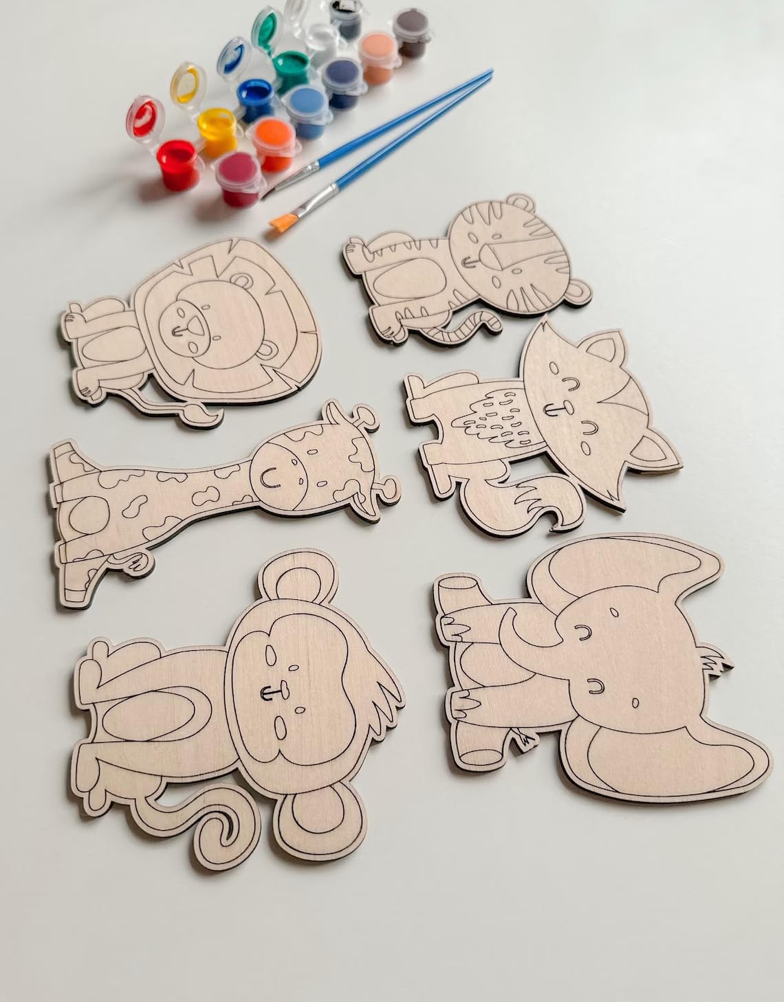 Set of animal-shaped wooden cutouts with paint supplies on a light background