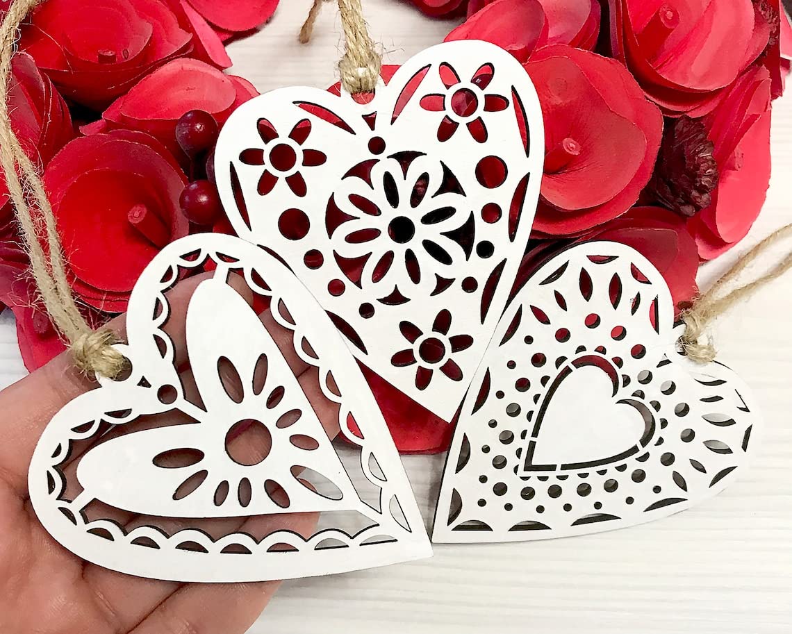 Three white heart-shaped decorations with floral patterns on a red floral background
