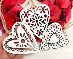 Three white heart-shaped decorations with floral patterns on a red floral background