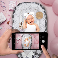 Baby lying in a crib with a phone capturing the moment on a pink background