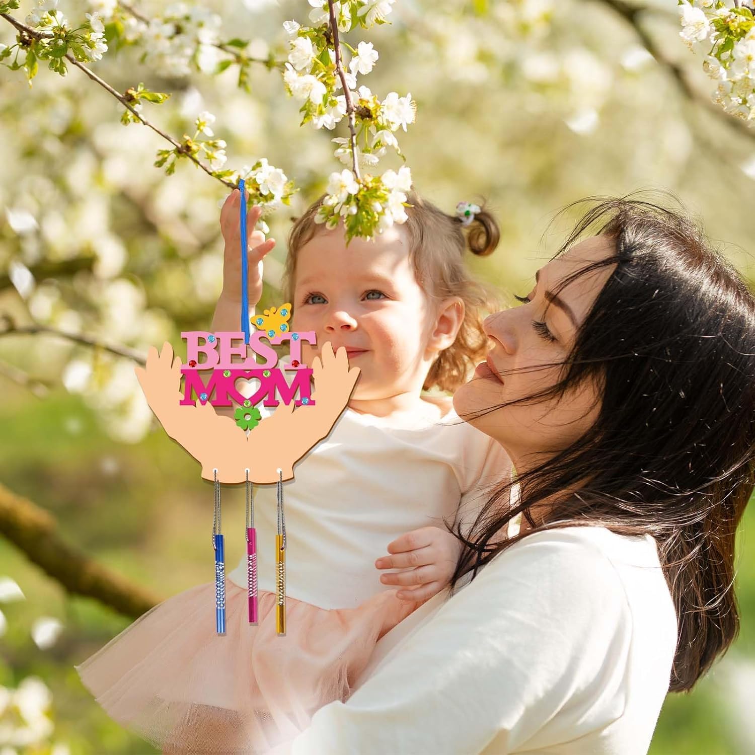 Woman holding a child with a 'Best Mom' sign in front of cherry blossom trees