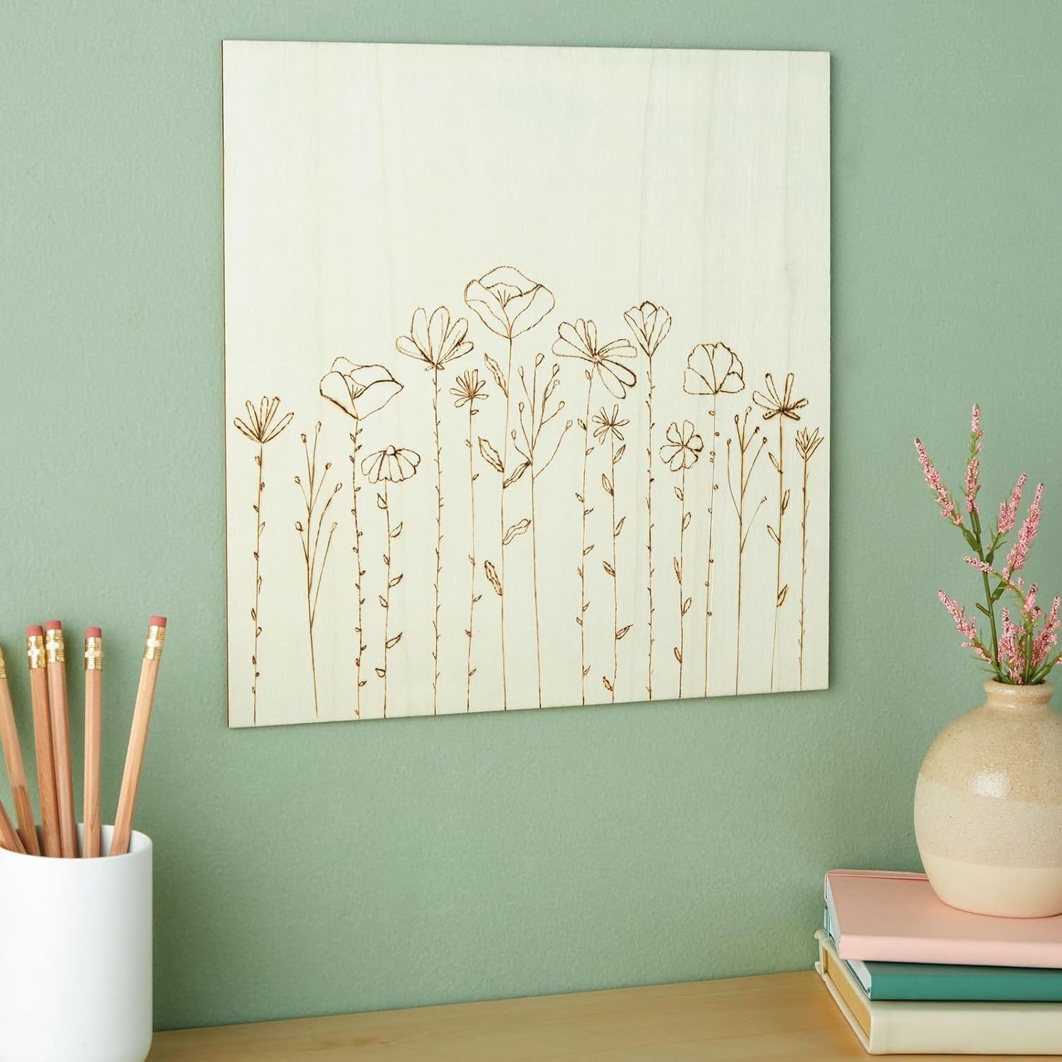 Decorative wall art with floral patterns on a green wall, next to a vase and books.