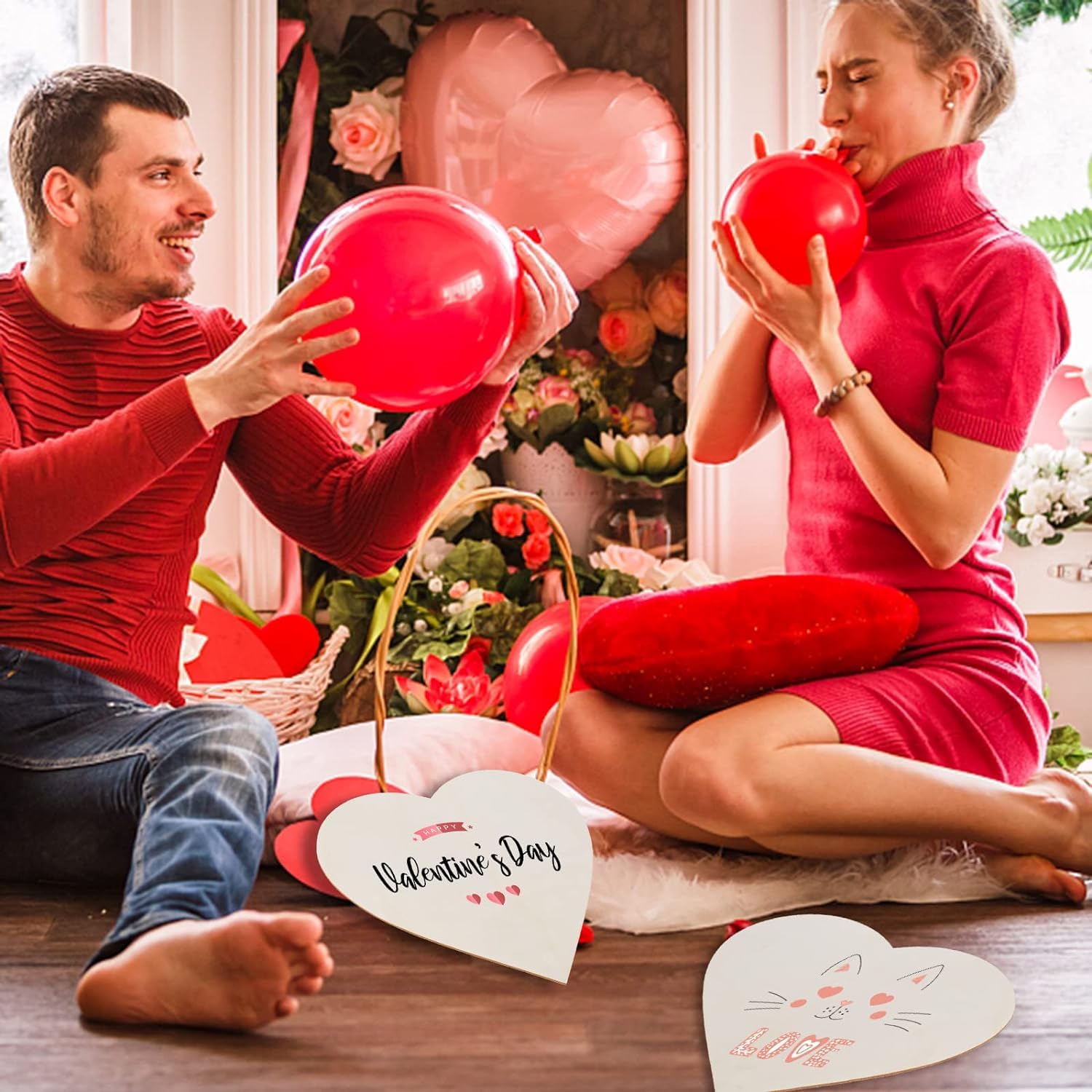 Man and woman holding red balloons in a decorated room with Valentine's Day decorations.