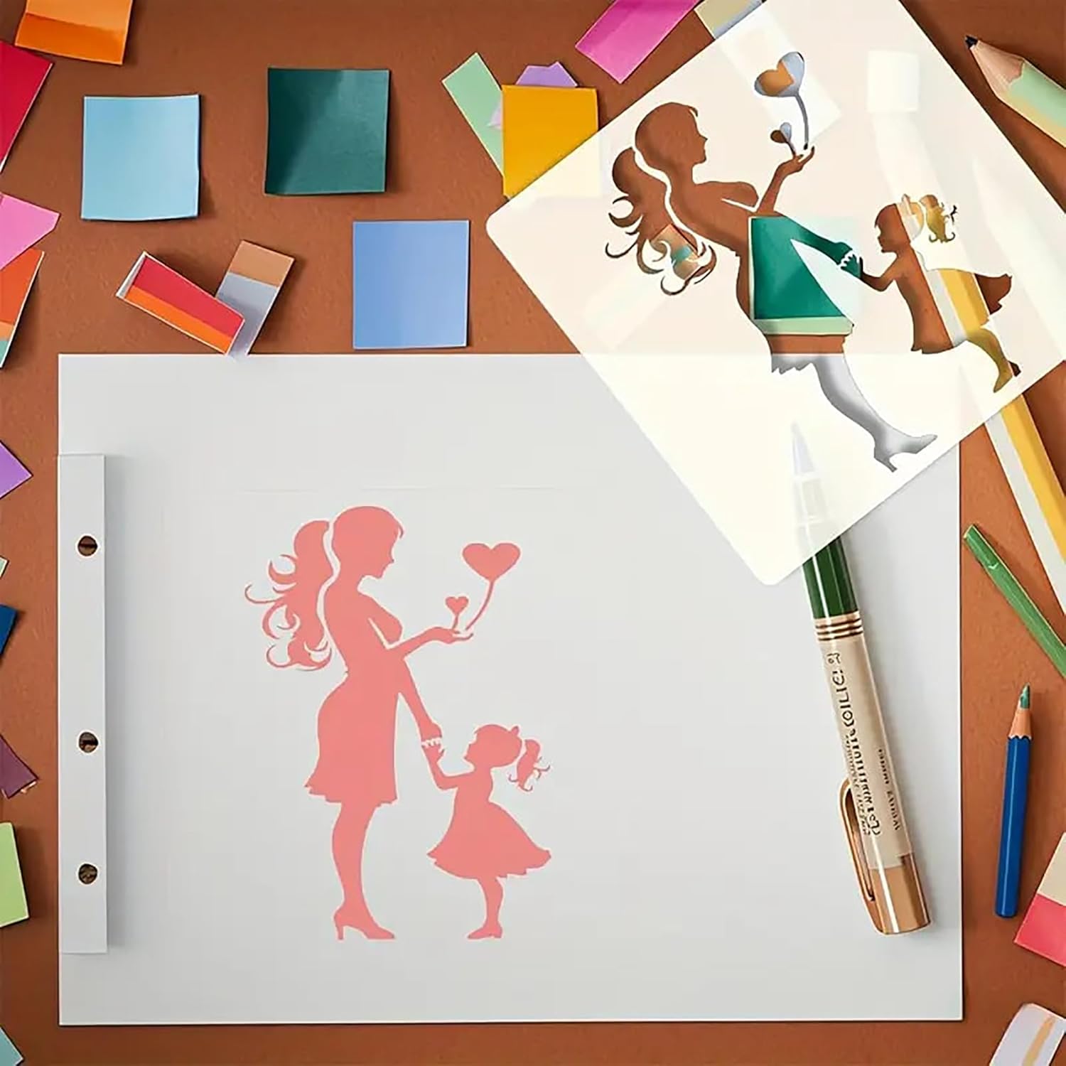 Paper cutouts of a mother and child with a heart, on a brown surface with markers and pencils.