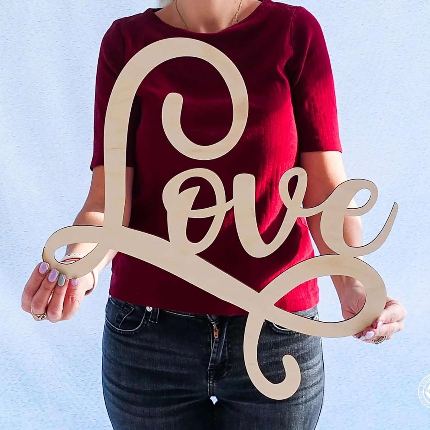 Person holding a wooden 'LOVE' sign against a light blue background