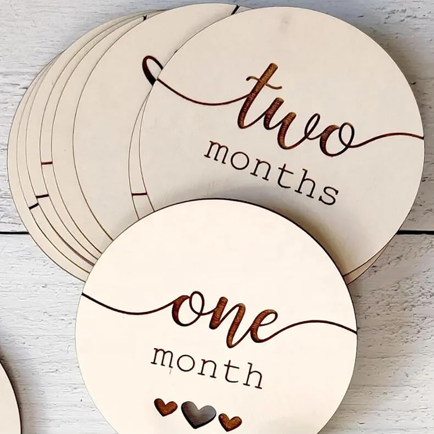 Wooden circular milestones with 'one month' and 'two months' text on a light wooden surface.