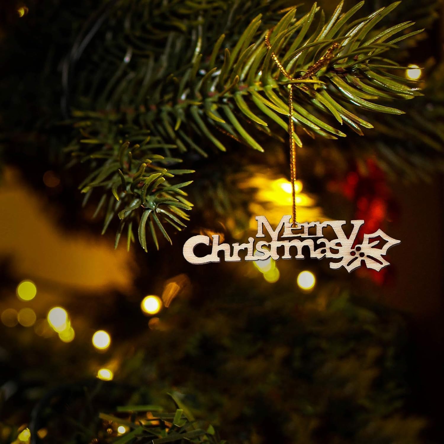 Merry Christmas ornament hanging on a decorated tree with blurred lights in the background