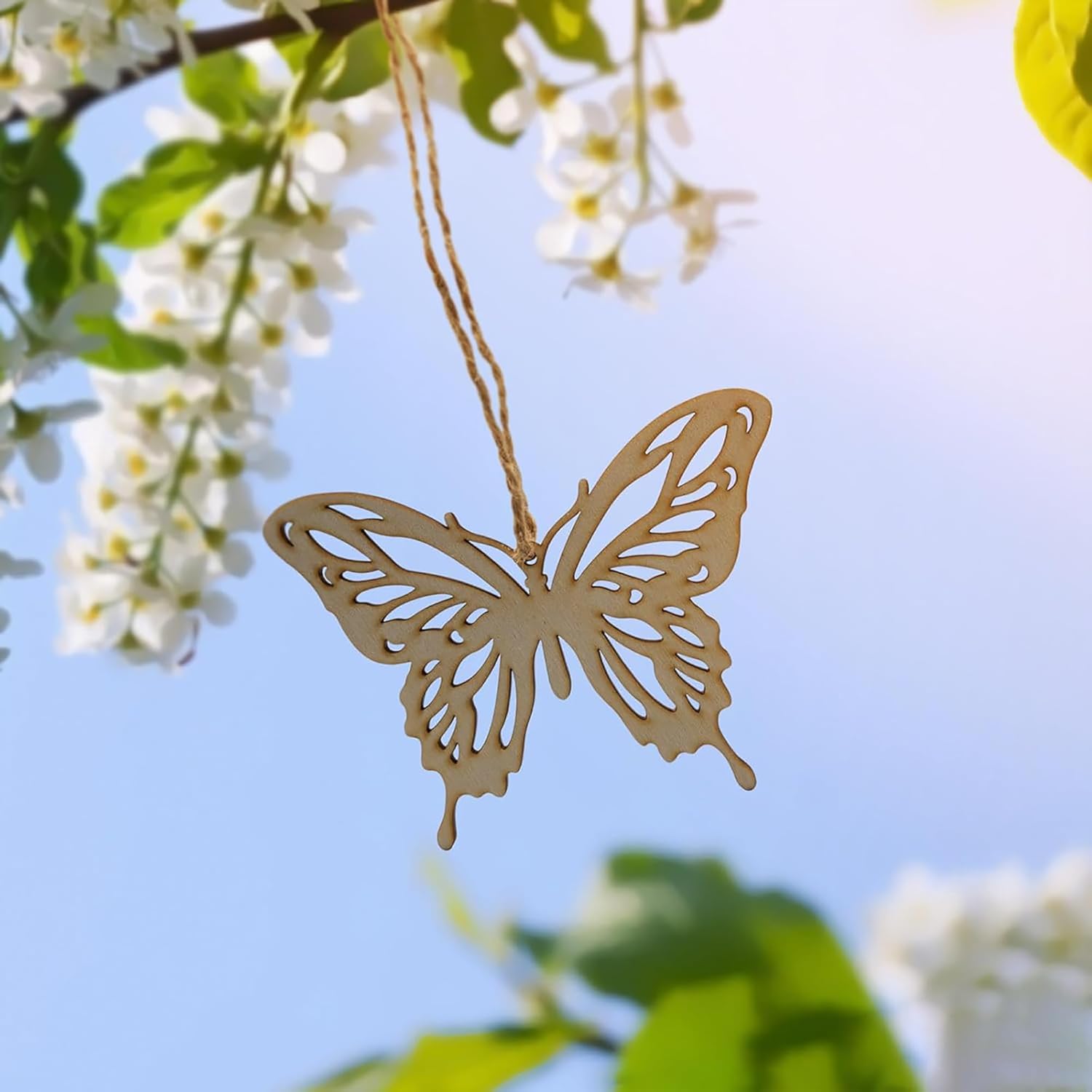 Gold butterfly-shaped pendant hanging from a branch with white flowers and green leaves.