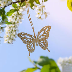 Gold butterfly-shaped pendant hanging from a branch with white flowers and green leaves.