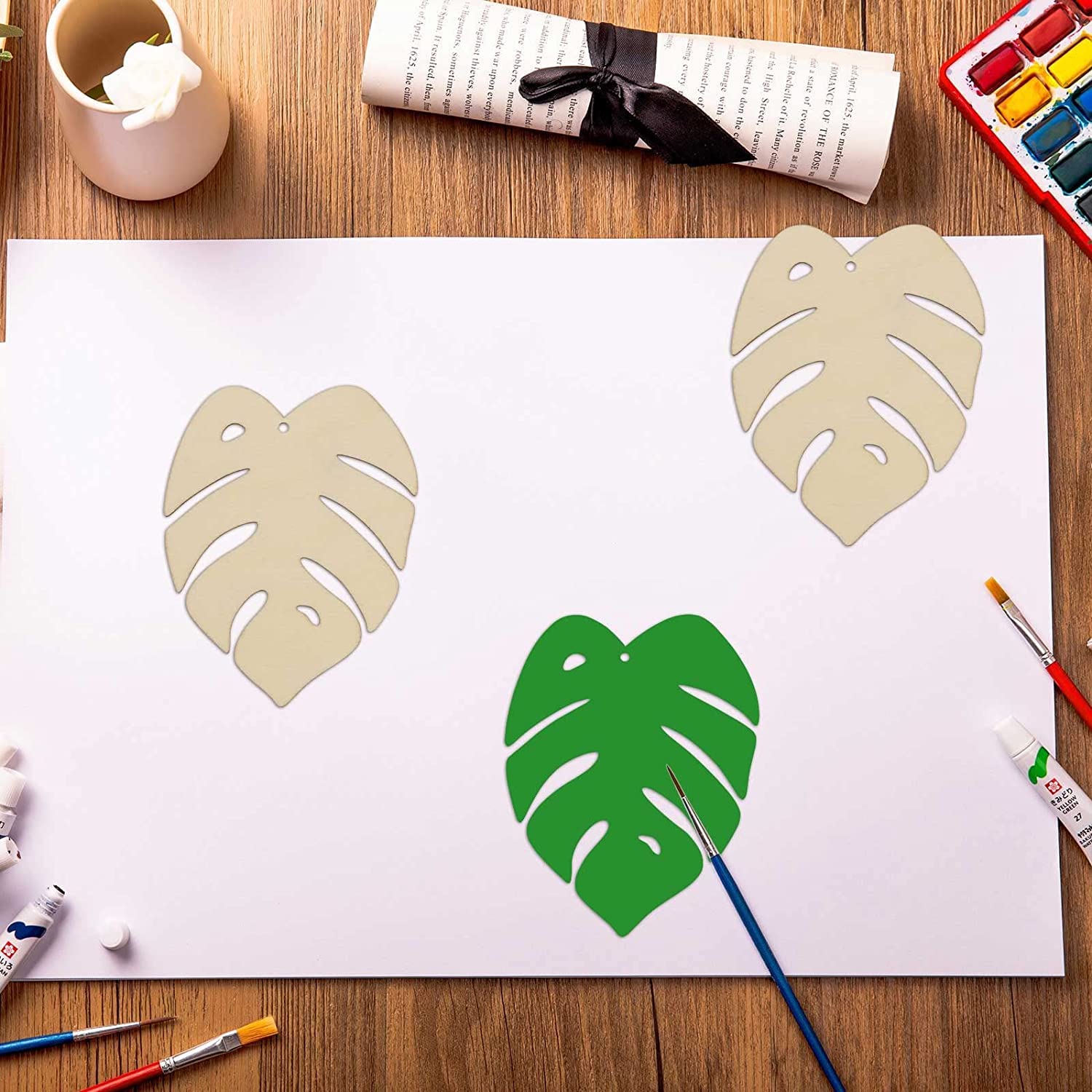 Artistic depiction of tropical leaves on a white sheet with painting tools around.