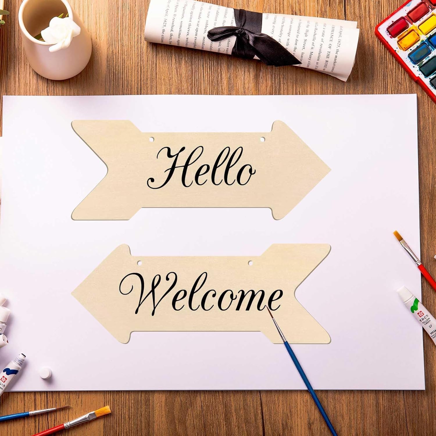 Wooden arrow-shaped signs with 'Hello' and 'Welcome' text on a table with art supplies.