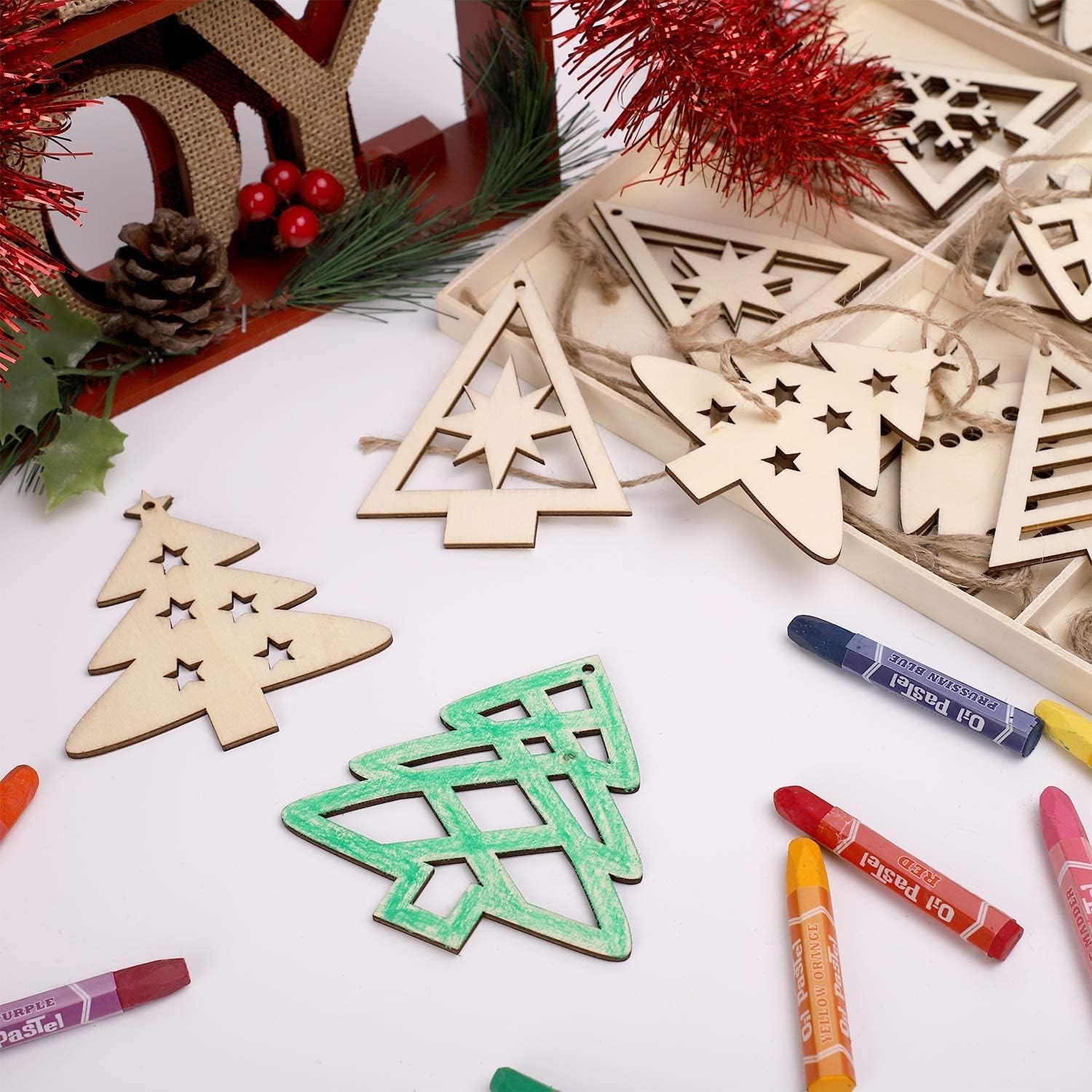 Wooden Christmas tree ornaments on a white surface with crayons and festive decorations.