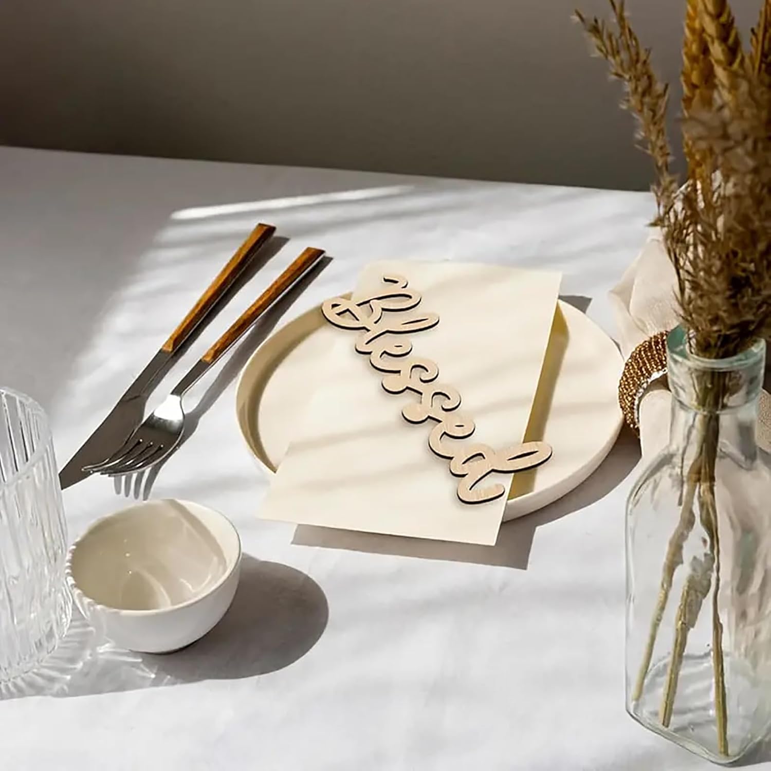 Table setting with a wooden 'Blessed' sign, plates, cutlery, and a vase with dried plants.