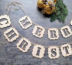 Wooden 'Merry Christmas' banner on a rustic wooden surface with gold ornaments and greenery.