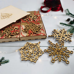 Wooden snowflake ornaments with packaging on a white surface with Christmas decorations.