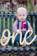 Child holding a wooden 'one' sign outdoors