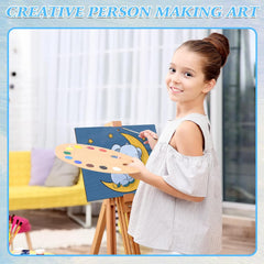 Young girl painting with a smile, holding a palette and a canvas with a blue background.