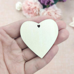 Heart-shaped wooden pendant held in a hand with flowers in the background