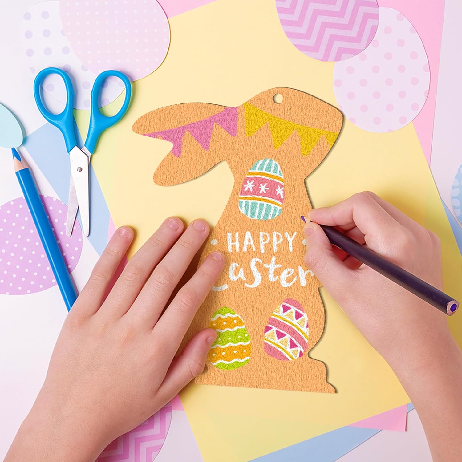 Child's hands coloring a paper Easter bunny with colorful eggs and 'Happy Easter' text on a pink background.