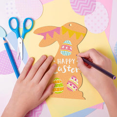 Child's hands coloring a paper Easter bunny with colorful eggs and 'Happy Easter' text on a pink background.