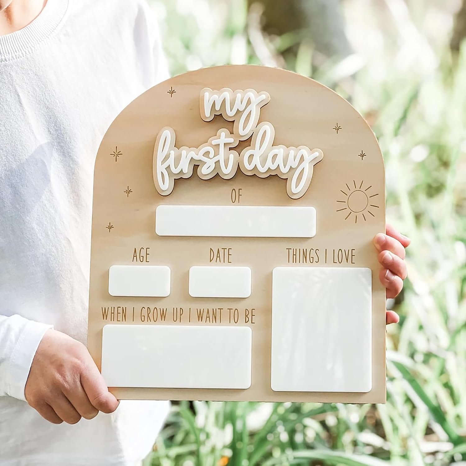 Wooden plaque with 'my first day' text held by a person against a blurred natural background