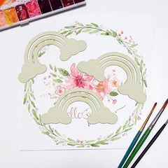 Artistic watercolor design of rainbows and flowers with paintbrushes and watercolor pan on a white background